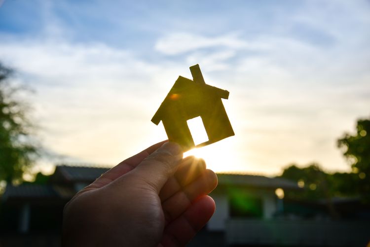 Mann hält kleines Holzhaus in der Hand mit Sonnenaufgang im Hintergrund