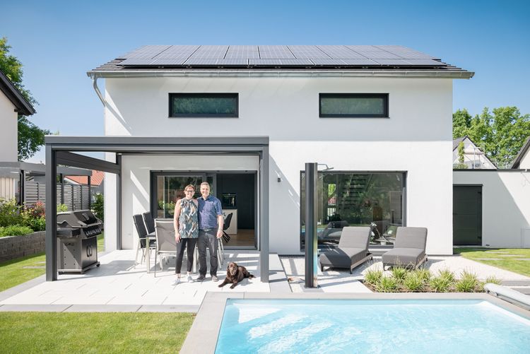 Bauherren auf der Terrasse ihres Einfamilienhauses mit Garten und Pool