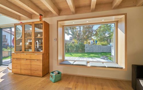 Das Sitzfenster des modernen Holzhauses im Landhausstil mit Mischfassade aus Holz und mineralischem Außenputz und vielen Glaselementen