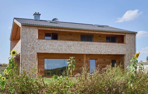 Modernes Holzhaus mit Holzverschindelung aus Tannenholz und geschützem Balkon- und Terrassenbereich