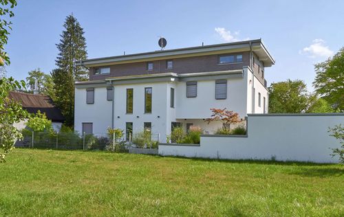 Moderner Wohnungsbau aus Holz mit Mischfassade aus Außenputz und Holz und Flachdach auf drei Ebenen