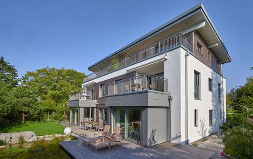 Moderner Wohnungsbau aus Holz mit Mischfassade aus Außenputz und Holz und Flachdach auf drei Ebenen