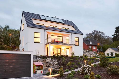 Modernes Fertighaus in Hanglage mit Garten und Abendbeleuchtung