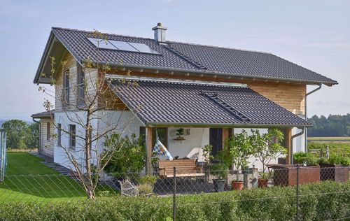 Die überdachte Terrasse des traditionellen Holzhauses mit Mischfassade aus Lärchenholz und Putz, mit flachem Satteldach und hohem Kniestock