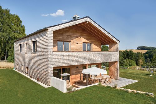 Modernes Holzhaus mit Holzverschindelung aus Tannenholz und geschützem Balkon- und Terrassenbereich