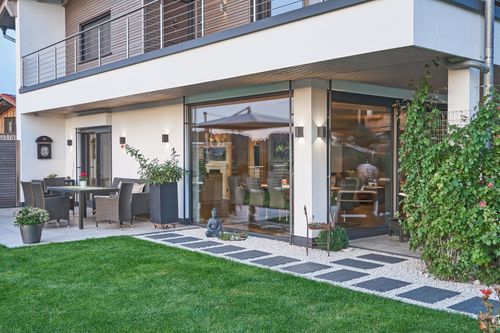 Die überdachte Terrasse des traditionellen Holzhauses mit Mischfassade aus Lärchenholz und Putz, flachem Satteldach und hohem Kniestock