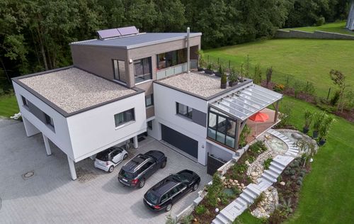 Modernes Holzhaus im Bauhausstil mit drei Gebäudetrakten, zwei davon mit mineralischem Außenputz und Flachdach, einer mit Holzfassade aus Fichtenholzbohlen und Pultdach