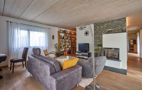 Das Wohnzimmer des modernen Holzhauses im Bauhausstil mit drei Gebäudetrakten, zwei davon mit mineralischem Außenputz und Flachdach, einer mit Holzfassade aus Fichtenholzbohlen und Pultdach